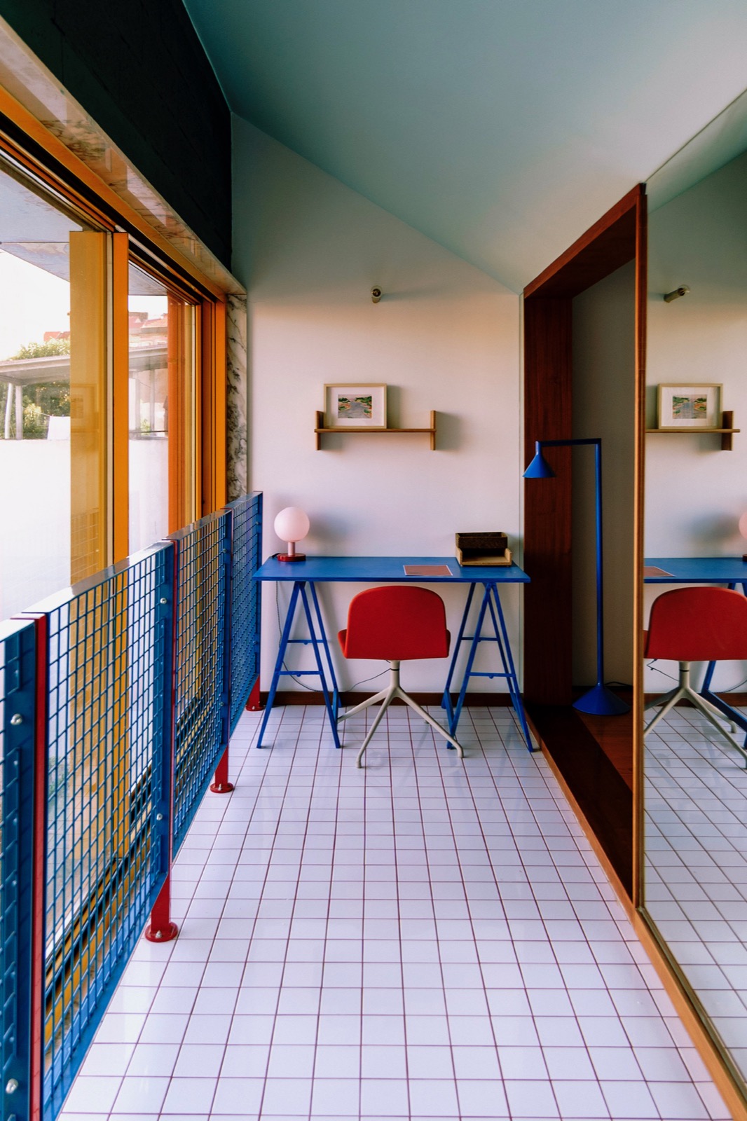 A bright tiled workspace at MAD House with a blue desk and balcony railing