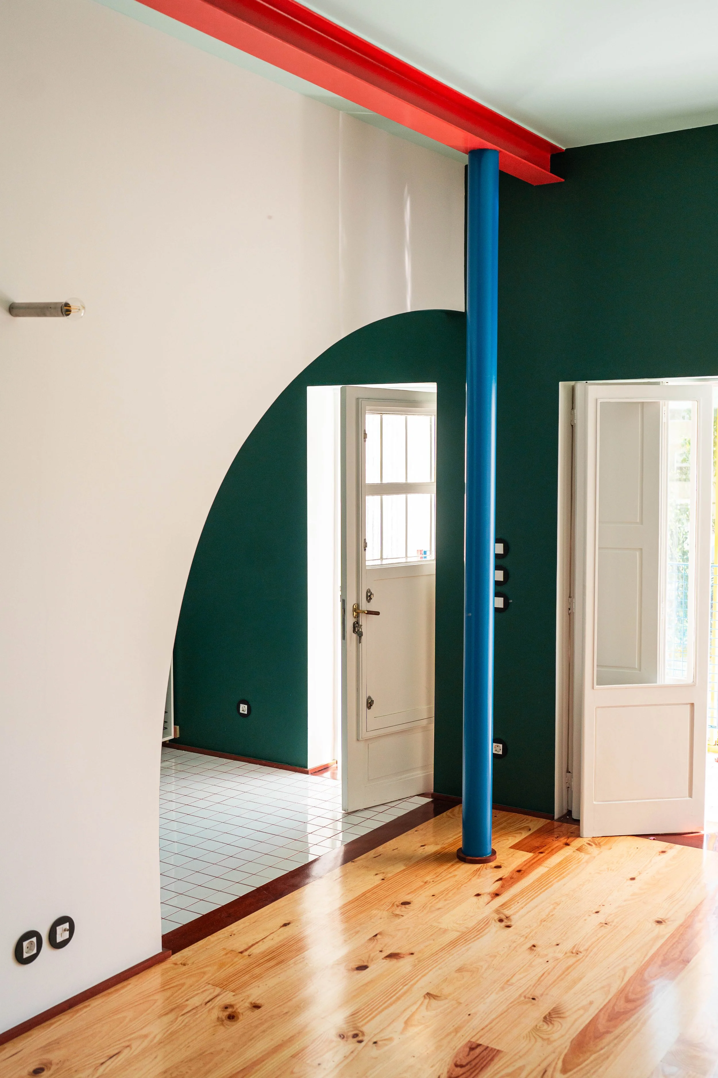 The colorful interior of MAD House in Porto, with an arched green wall and blue column